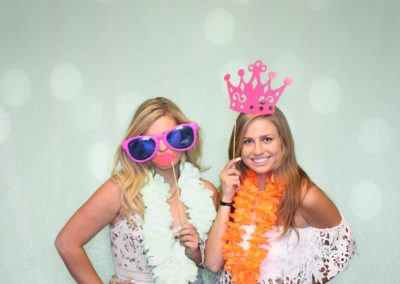 Two girls in photo booth with glasses, leis, and other props