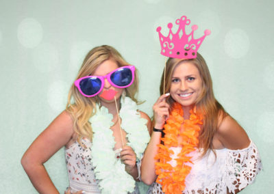 Two girls in photo booth with glasses, leis, and other props