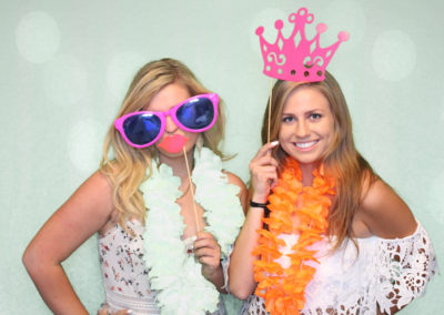 Two girls in photo booth with glasses, leis, and other props